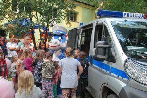 Radiowóz policyjny w pobliżu którego stoi maskotka będzińskiej policji smoczyca Klara oraz grupa dzieci