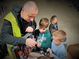 Na zdjęciu technik kryminalistyki pokazuję dzieciom swoją walizkę i wyciąga lupę.
